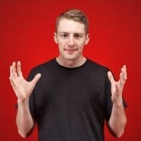 gestures - Serious angry young male model dressed in a black t-shirt on a red background, holding two hands up in a sign of indignation, discontent frowning face and trying to sink in the bad news